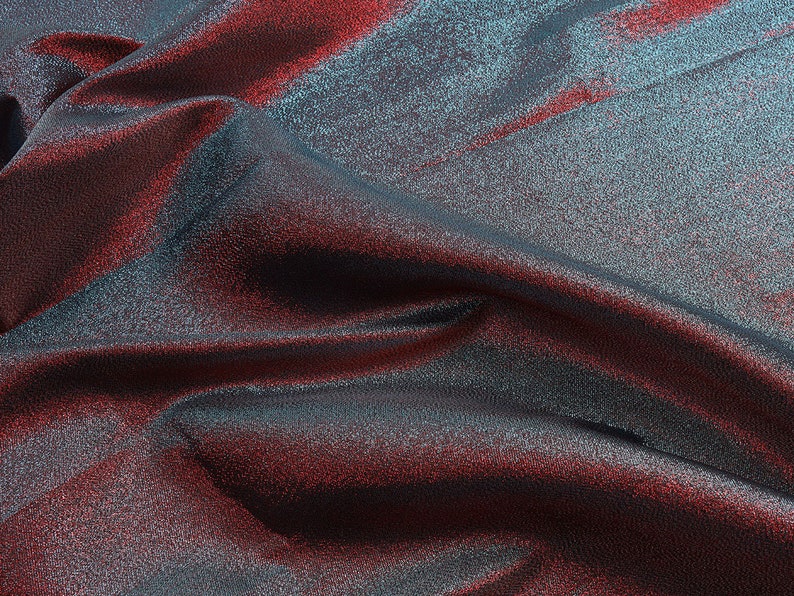 May include: Close-up of a shimmering fabric with a blue and red iridescent sheen. The fabric is draped and folded, creating soft, flowing lines.
