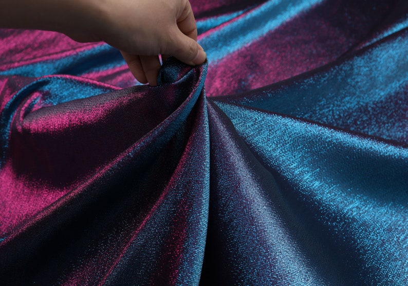 May include: Close-up of iridescent fabric with a blue and purple color gradient. The fabric is smooth and shiny, with a subtle texture.