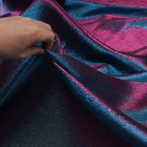 May include: Close-up of iridescent fabric with a blue and pink color gradient. The fabric has a subtle shimmer and a textured surface.