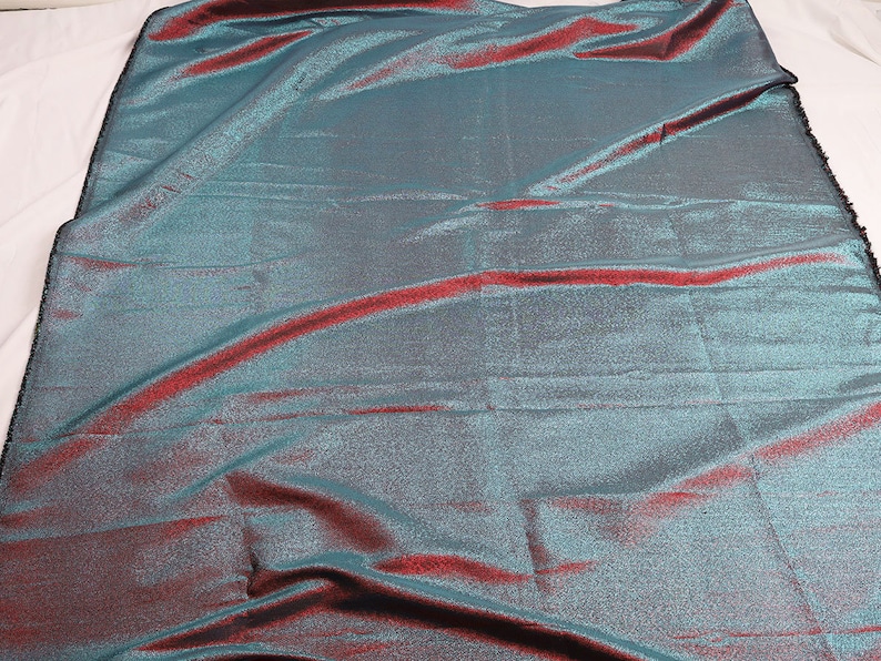 May include: A teal and burgundy iridescent fabric with a subtle shimmer. The fabric has a woven texture and a slightly crinkled appearance.