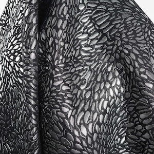 Può includere: Tessuto nero con un motivo goffrato metallico argentato a forma di vortici.