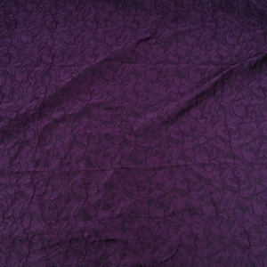 Pu&ograve; includere: Un pezzo di tessuto viola scuro con un motivo floreale in rilievo. Il tessuto &egrave; drappeggiato, mostrando pieghe e ombre. Il colore &egrave; una tonalit&agrave; ricca e scura di viola.