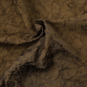 May include: A close-up shot of brown fabric with a floral design. The material has a textured surface with raised floral patterns. The folds and shadows create depth, highlighting the intricate details of the embossed pattern.