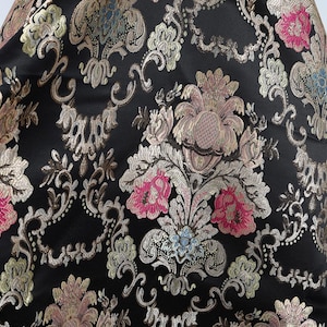 May include: Black fabric with a gold, pink, and blue floral pattern. The fabric has a brocade texture.