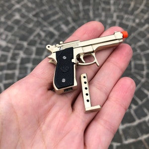 May include: A gold-colored toy pistol with a black grip and an orange tip, with a detached magazine. The toy gun is a replica of a handgun.