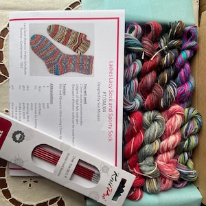 May include: A kit for knitting a lacy sock and a sporty sock. The kit includes yarn in various colours, double pointed needles, and instructions. The instructions include the text "Ladies Lacy Sock and Sporty Sock PT/SM/04 Designed by Sue Morgan".