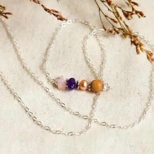 Peut inclure: Un collier en chaîne argent avec un pendentif composé d'une pierre rose, violette et marron avec un accent de perle.