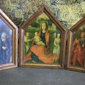 May include: A wooden triptych with three panels, each featuring a religious painting. The center panel depicts the Virgin Mary holding the baby Jesus, flanked by two angels. The left panel shows a woman in blue robes, and the right panel shows a man in red robes.