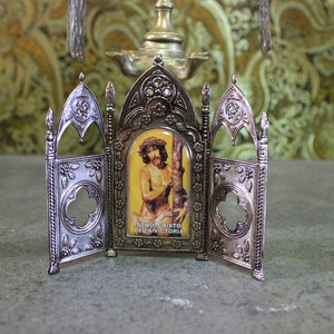 May include: A silver-colored, ornate, three-panel display stand with a small image of a man with a crown of thorns. The image is labeled "SEMI CRISTO DELA VICTORIA".
