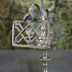 May include: A brass candlestick with a decorative design featuring a cross and a figure. The candlestick has a round base and a tall, slender stem.