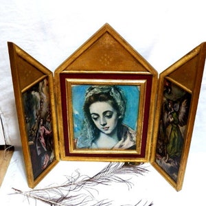 May include: A three-panel wooden frame with gold leaf accents. The center panel features a painting of a woman with a blue background. The side panels feature paintings of angels.