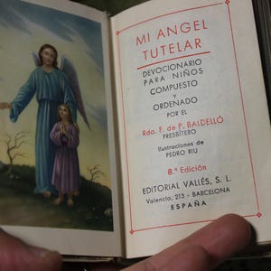 May include: Open book with the title "MI ANGEL TUTELAR" in Spanish. The left page features an illustration of an angel and a child. The right page has text in Spanish, including the author's name and the publisher's address.