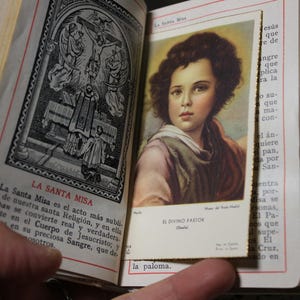 May include: An open, antique book with gold-colored edges and a decorative cover. The left page features a black and white illustration and text in Spanish. The right page displays a color image of a young person. The text "EL DIVINO PASTOR" is visible.