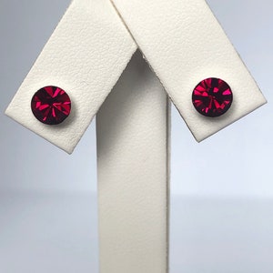 May include: A pair of small, round, red stud earrings with a faceted design.