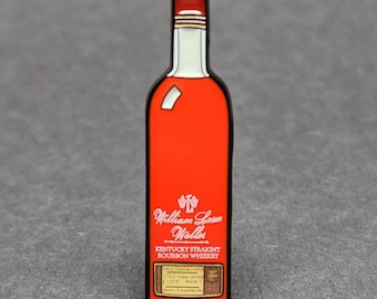 Könnte beinhalten: Eine rote Emaille-Anstecknadel in Form einer Flasche William Larue Weller Kentucky Straight Bourbon Whiskey. Die Anstecknadel hat ein weißes Etikett mit schwarzem Text und einem goldenen Rand.