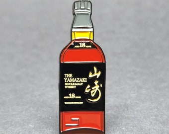 May include: A gold and black enamel pin shaped like a bottle of Yamazaki 18 year old single malt whisky. The bottle is red and has a gold label with the text "The Yamazaki Single Malt Whisky Aged 18 Years" and a gold Japanese character.