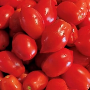 May include: A close-up shot of a pile of bright red Roma tomatoes. The tomatoes are oval-shaped with a smooth, shiny surface, and some have small water droplets. The tomatoes are ripe and ready to eat.
