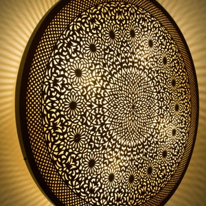Pode incluir: Um candeeiro de teto redondo e decorativo com um design intrincado cortado a laser. O candeeiro é feito de metal e tem um acabamento dourado quente.