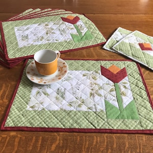 May include: Set of green and white quilted placemats with a red and orange tulip design. The placemats have a burgundy border. There are also two matching coasters.