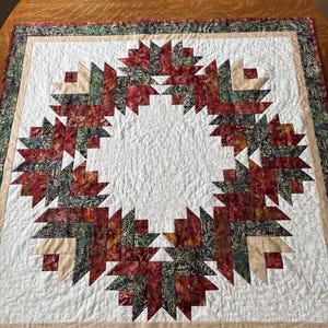 May include: A white quilt with a red, green and beige patterned border. The centre of the quilt features a circular design of red, green and beige triangles.