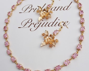 May include: A gold-toned jewelry set featuring a necklace and earrings. The necklace and earrings are adorned with pink rectangular gemstones and floral accents. The background has the words "Pride and Prejudice" in a script font.