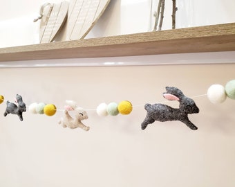 Puede incluir: Guirnalda decorativa con conejitos de fieltro y bolas de fieltro de colores. La guirnalda incluye conejitos grises con orejas rosas y conejitos de color claro, intercalados con bolas amarillas, blancas y verdes. Ideal para decoraciones de Pascua.