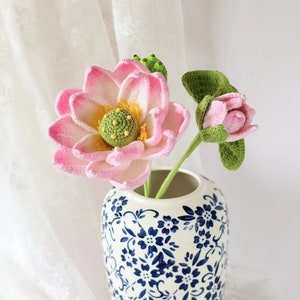 May include: A pink and green crocheted lotus flower arrangement in a white and blue floral patterned vase.