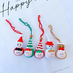 May include: Five crocheted ornaments with different festive themes. The ornaments are red, green, white, and brown. Each ornament has a smiling face and a different hat. The ornaments are hanging from red, green, white, and brown strings. The text "Happy day" is written in black at the top of the image. The text "Sleep when tired and smile when awake Let's fall in love" is written in black at the bottom of the image.