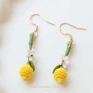 Puede incluir: Pendientes de lim&oacute;n de ganchillo con flores blancas y tallos verdes. Los pendientes son de color dorado y cuelgan de la oreja.