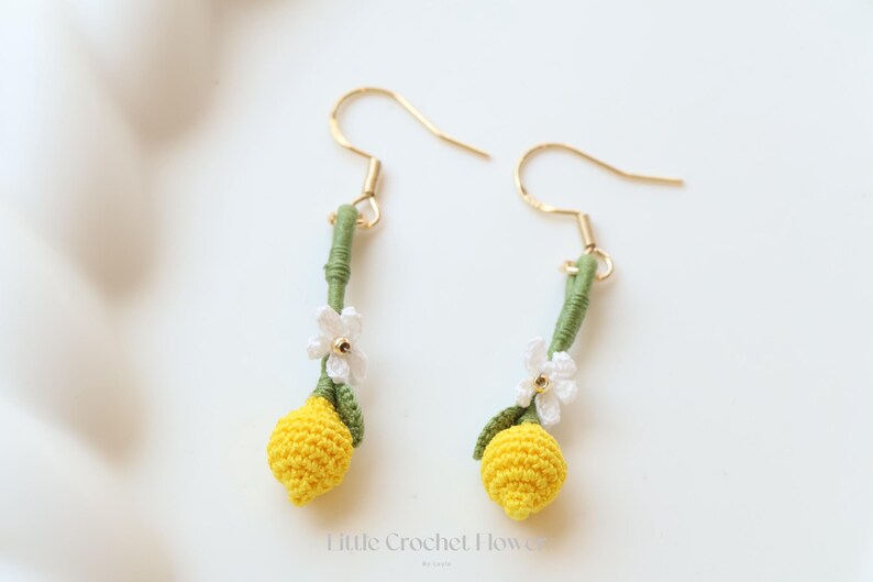 Puede incluir: Pendientes de lim&oacute;n de ganchillo con flores blancas y tallos verdes. Los pendientes son de color dorado y cuelgan de la oreja.