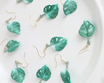 May include: A set of eight crocheted green and white leaf earrings with gold hooks. The earrings are arranged on a white surface. The text "Little Crochet Flower By Layla" is at the bottom of the image.