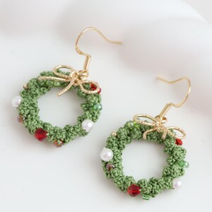 May include: A pair of green crocheted Christmas wreath earrings with red and white beads and gold hooks.