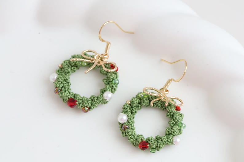 May include: A pair of green crocheted Christmas wreath earrings with red and white beads and gold hooks.