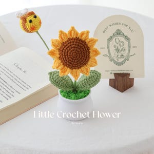 May include: A handmade crochet sunflower with a brown center and yellow petals, in a white pot with green leaves. A crochet bee is on a stem. A card with text "Best Wishes For You" is in the background. The text "Little Crochet Flower" is at the bottom.