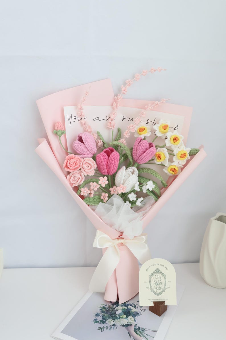 May include: A pink and white crocheted flower bouquet with a card that says "You are sunshine". The bouquet is wrapped in pink tissue paper and tied with a white ribbon.