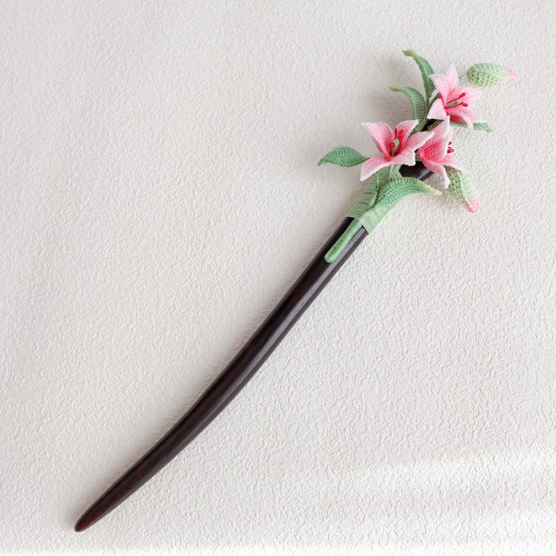 May include: A dark brown wooden hair stick with a decorative floral design. The flowers are pink with green leaves and accents. The hair accessory is a unique and elegant addition to any hairstyle.