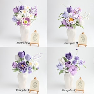 May include: Four arrangements of crocheted flowers in white ribbed vases. Each bouquet features various shades of purple, lavender, and white blossoms, including tulips and peonies. Small wooden easels display cards labeled Purple 5, 6, 7, and 8.