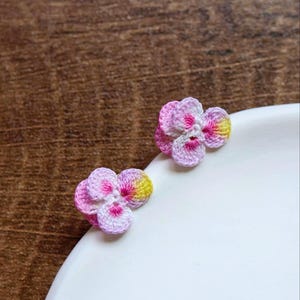 May include: Two small crocheted flower earrings in pink, white, and yellow.