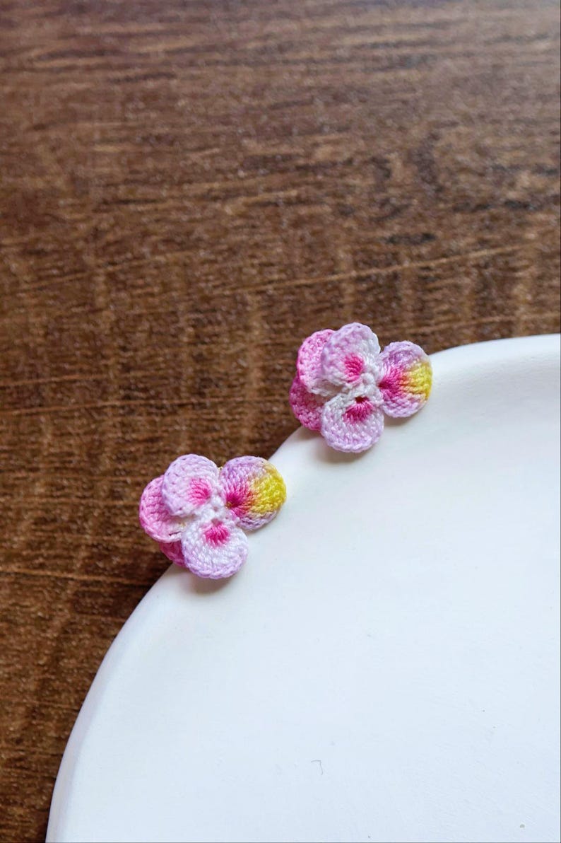 May include: Two small crocheted flower earrings in pink, white, and yellow.