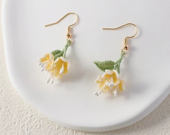 May include: A pair of delicate floral earrings with yellow and white crocheted flowers and green leaves hanging from gold hooks.