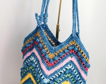 May include: A colorful crocheted tote bag with a blue, yellow, green, pink, and red chevron pattern. The bag has a blue crocheted strap and the text "Little Crochet Flower by Layla" is printed on the bottom.