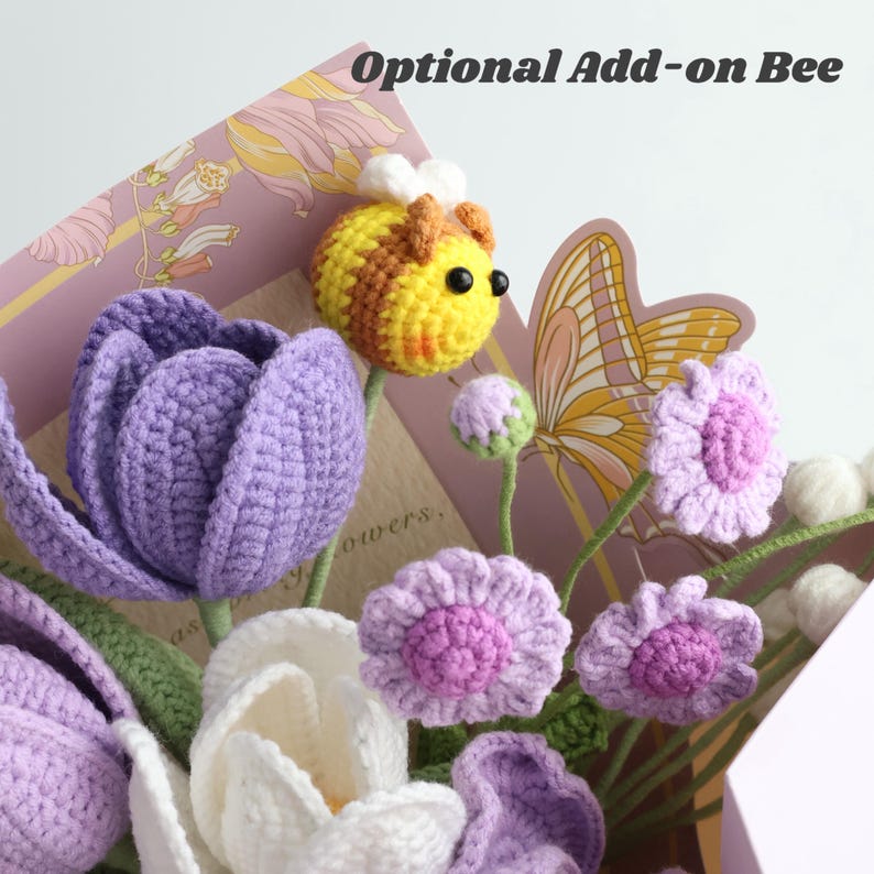 May include: A crochet flower bouquet featuring purple and white tulips, small light purple flowers, and a yellow and brown striped crochet bee with white wings. The text "Optional Add-on Bee" is visible at the top of the floral arrangement.