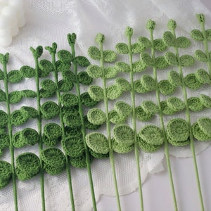 May include: Handmade crochet stems with green leaves. The stems are a light green color, and the leaves are a darker shade of green. The leaves are round and have a textured appearance. The stems are arranged in a row.