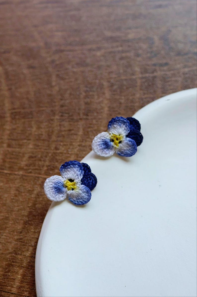 May include: A pair of small, crocheted flower earrings. The flowers are blue, white, and yellow.
