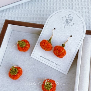 May include: Crocheted pumpkin earrings with green stems and gold hooks. The earrings are displayed on a white card with the text "Handmade with Love" and "Little Crochet Flower".