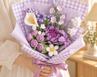 May include: A bouquet of crocheted flowers in shades of purple, lavender, and white, featuring roses, a calla lily, and a large chrysanthemum. The arrangement is wrapped in purple gingham paper and textured lavender paper, tied with a purple ribbon.