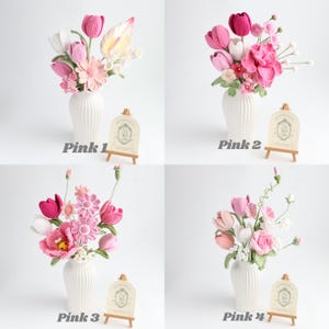 May include: Four arrangements of crocheted flowers in white ribbed vases, labeled Pink 1 through Pink 4. Each bouquet features various shades of pink and white yarn flowers, including tulips and daisies, displayed with a small wooden easel sign.