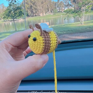 May include: A crocheted bee toy with yellow and brown stripes, white wings, and black eyes. The bee is hanging from a yellow string.
