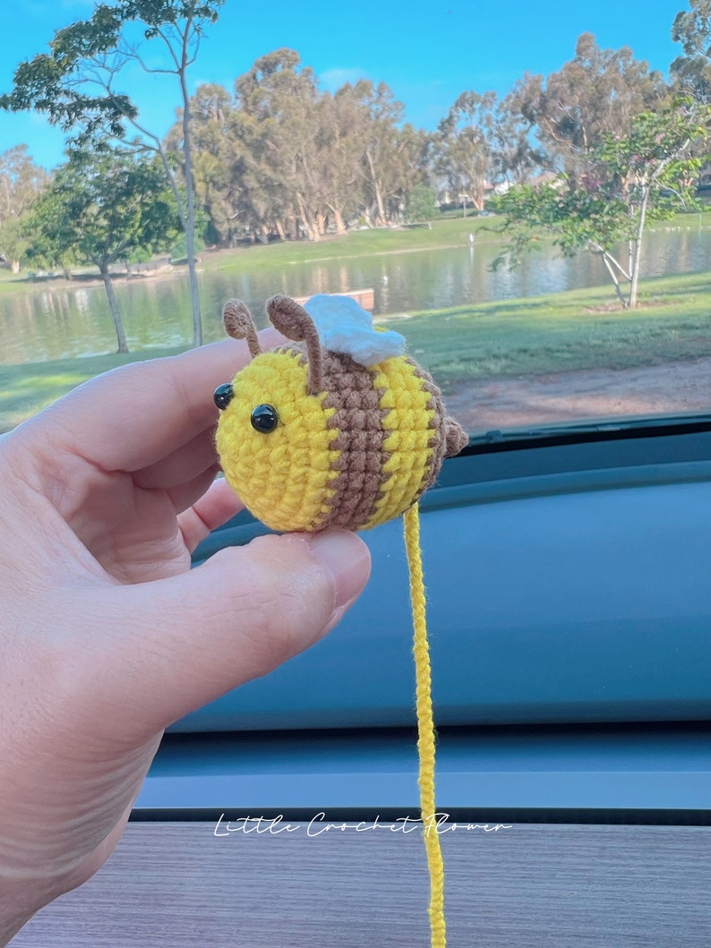 May include: A crocheted bee toy with yellow and brown stripes, white wings, and black eyes. The bee is hanging from a yellow string.
