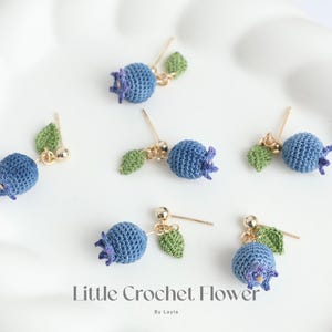 May include: Six pairs of crocheted blueberry earrings with gold posts and green leaves. The earrings are displayed on a white surface. The text "Little Crochet Flower" is written below the earrings.
